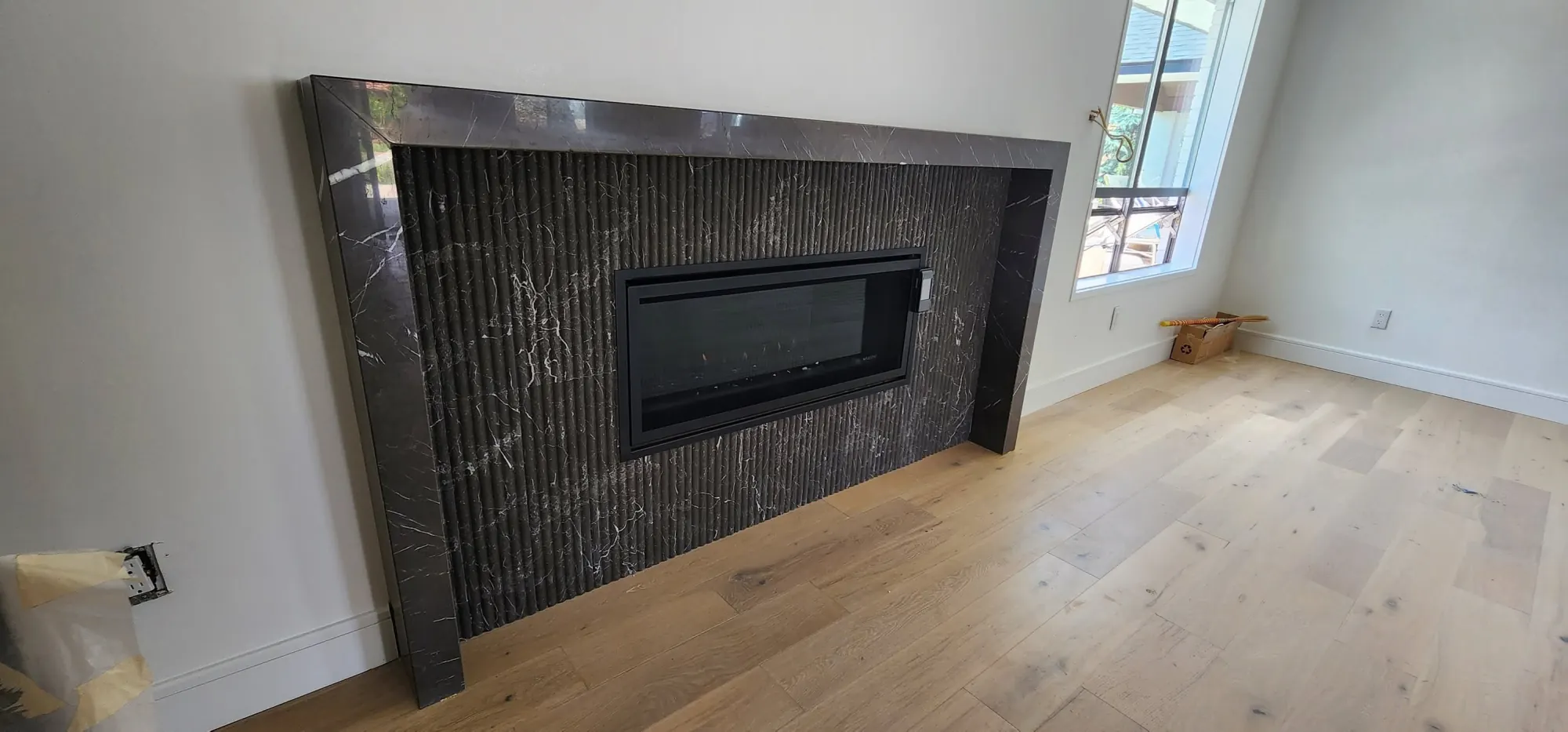 Linear fireplace surrounded by fluted dark stone and pale oak flooring