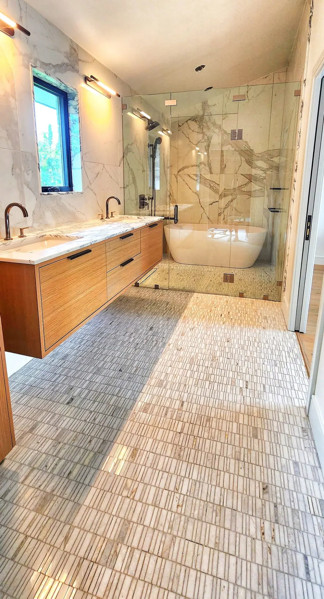 Warm wood vanity and marble-lined primary bathroom by Amni Renovations